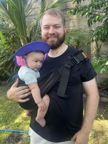 Vater trägt sein Baby in der schwarzen Vianaa Tragehilfe